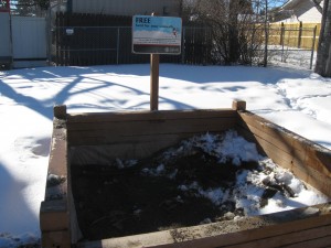 low wooden box outdoors looking like a sandbox, with a sign saying residents can take sand for their sidewalks