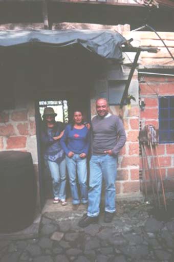 Angela, Patricia and Carlos outside Angela's wooden-and-brick hut