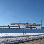 blue sky with snow in front and in the distance a giant crane building a bridge