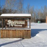 sign saying Pumphouse Theare, made of wood, with blue sky and trees behind, snow on the ground